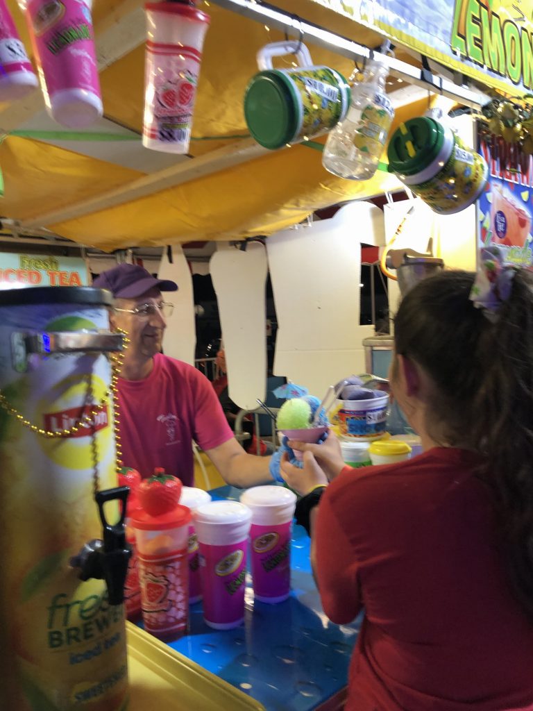 man handing out hawaiian ice cup to girl.